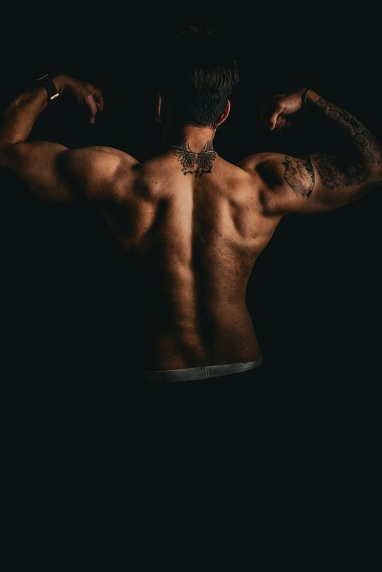 A back double-biceps pose shot in low light