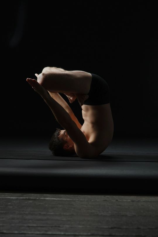 A curled recovery pose on a mat in a dark studio