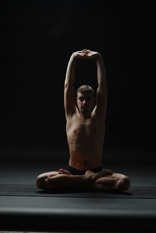 A seated overhead stretch in a dark studio